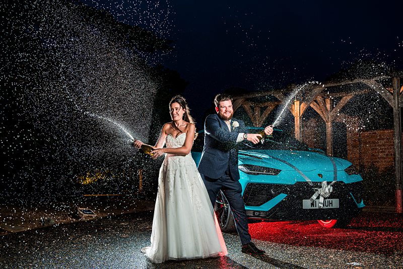 Couple celebrates with champagne spray by sports car.