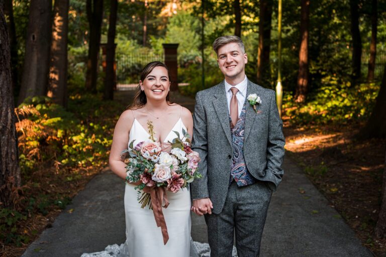 Smiling couple in wedding attire outdoors.