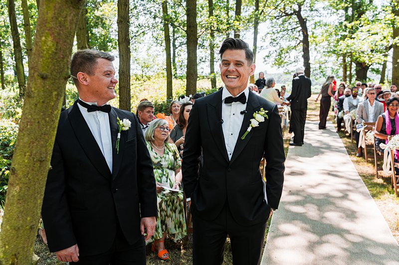 Outdoor wedding with two grooms smiling.