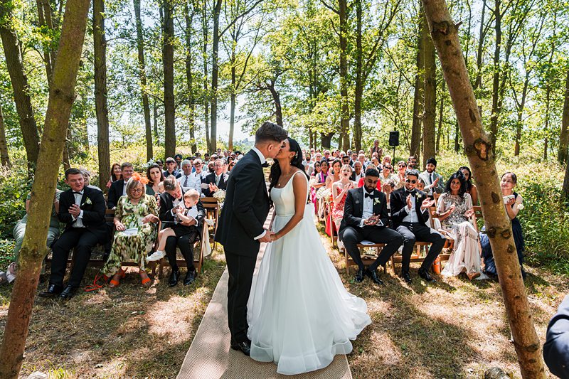 Bride and groom kiss at outdoor forest wedding ceremony.