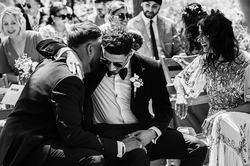 Groom hugging friend at outdoor wedding ceremony.