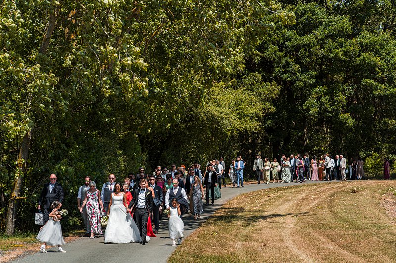 Wedding procession walking through a leafy path.