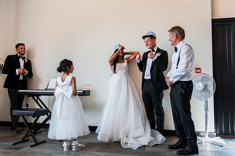 Wedding party laughing and wearing caps indoors.