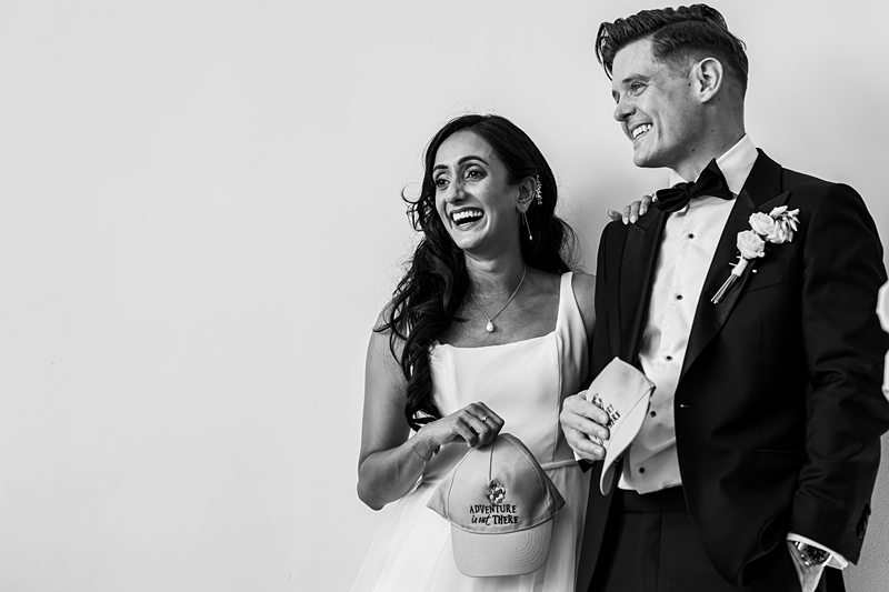 Smiling couple in wedding attire with cap.