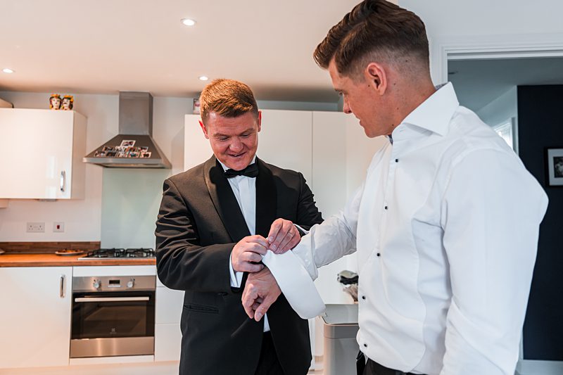 Men adjusting cufflinks in kitchen before event.