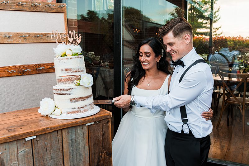 Couple cutting wedding cake together outdoors.