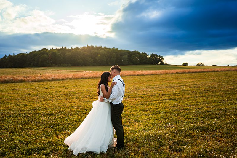 Newlyweds embrace in sunset field, romantic scene.