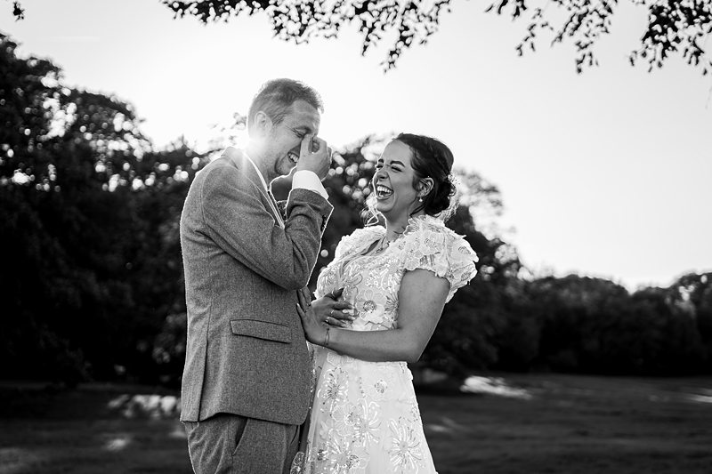 Couple laughing in wedding attire outdoors.