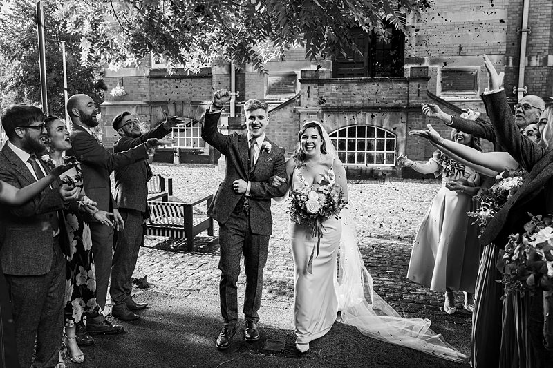 Newlyweds exit wedding ceremony amidst cheering guests.