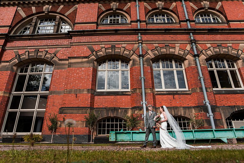 Bride and groom outside brick building, smiling.