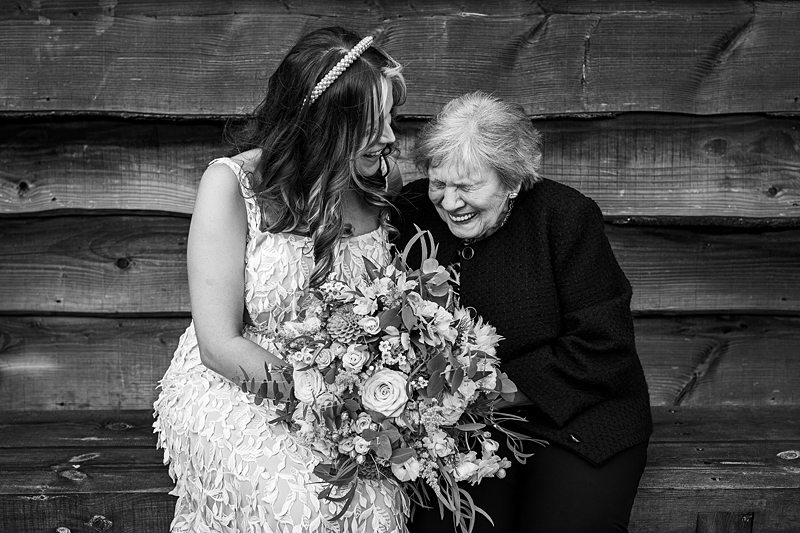 Bride and guest sharing a laugh, holding bouquet.