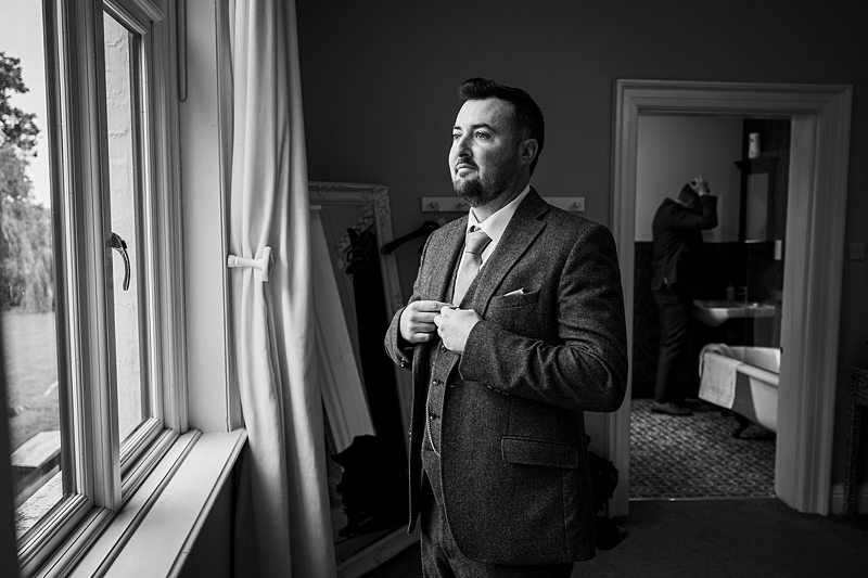 Man in suit looking out window before event.