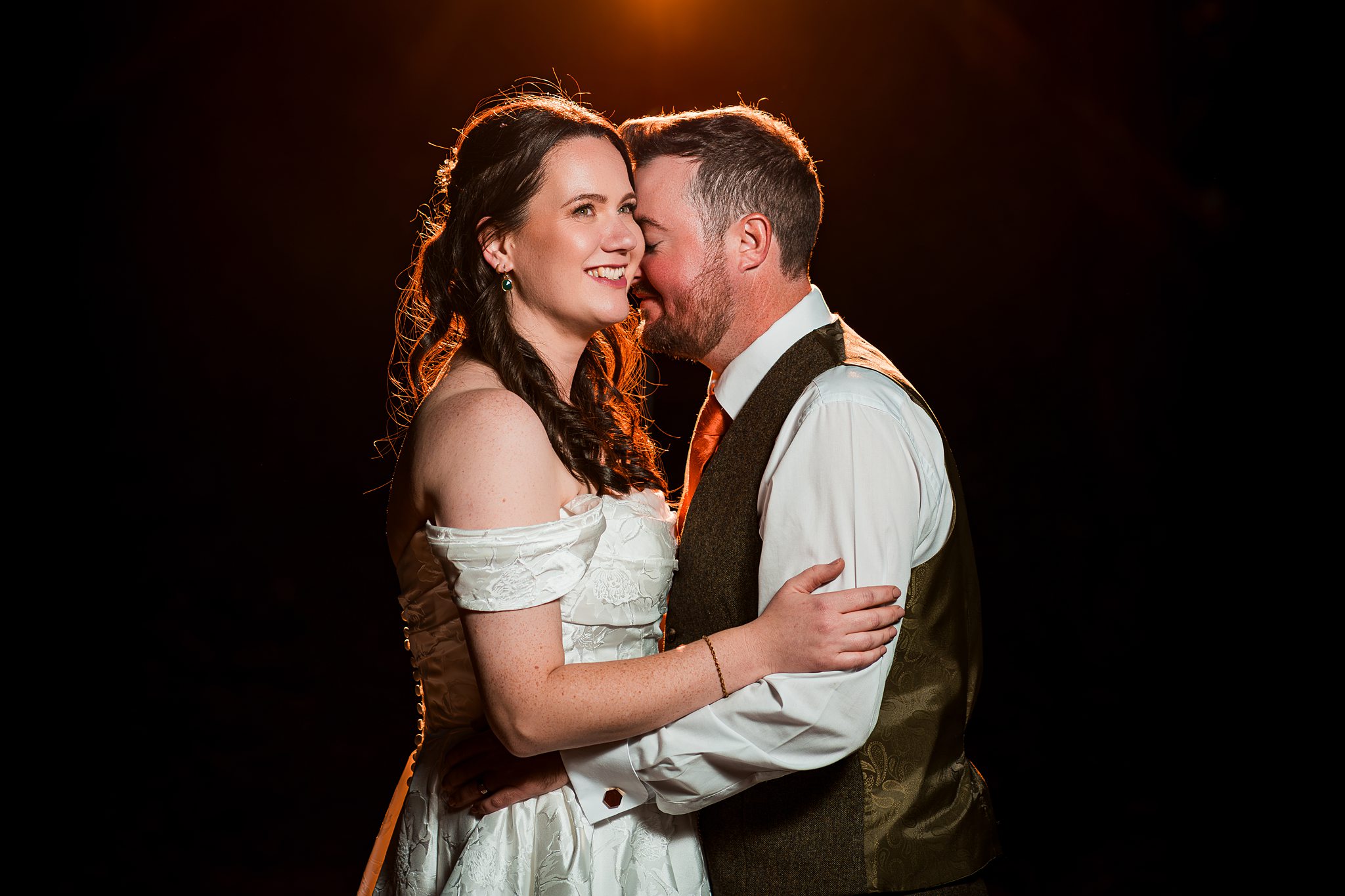 Smiling couple embrace under romantic lighting.