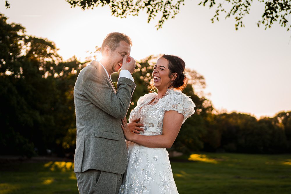 Bride and groom laughing in sunlit park