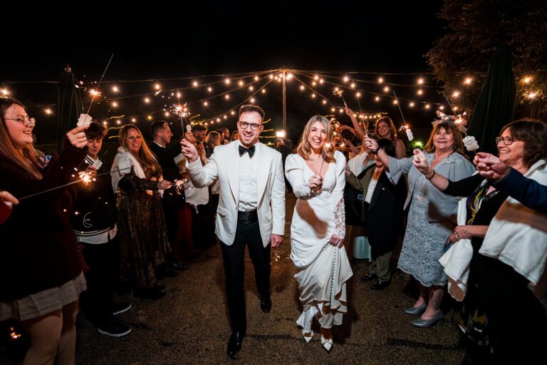 Wedding couple celebrates with guests and sparklers at night.