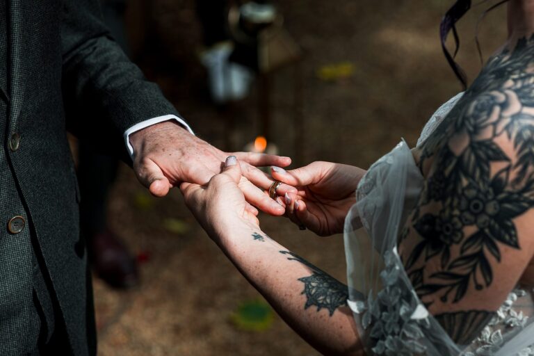Tattooed bride placing ring on groom's finger.